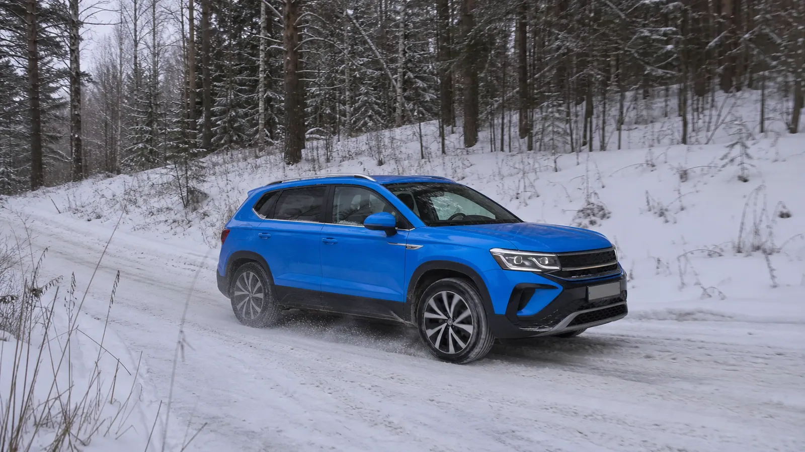 Синий Volkswagen Taos едет по заснеженной лесной дороге